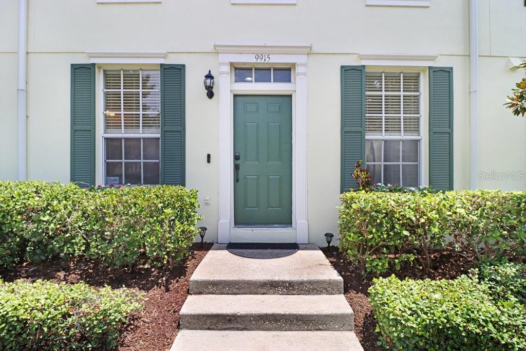 A green front door is centered between two windows with green shutters and landscaping — 9915 NEW PARKE ROAD, TAMPA, FL