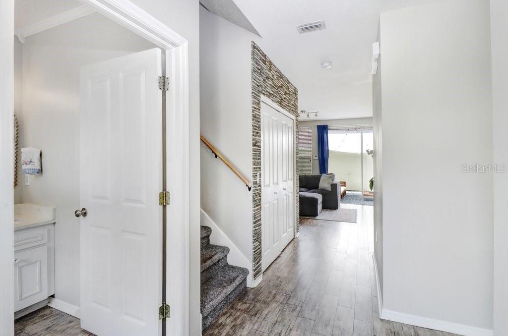 An interior hallway features wood-look flooring, a carpeted staircase, and a stone accent wall — 9915 NEW PARKE ROAD, TAMPA, FL