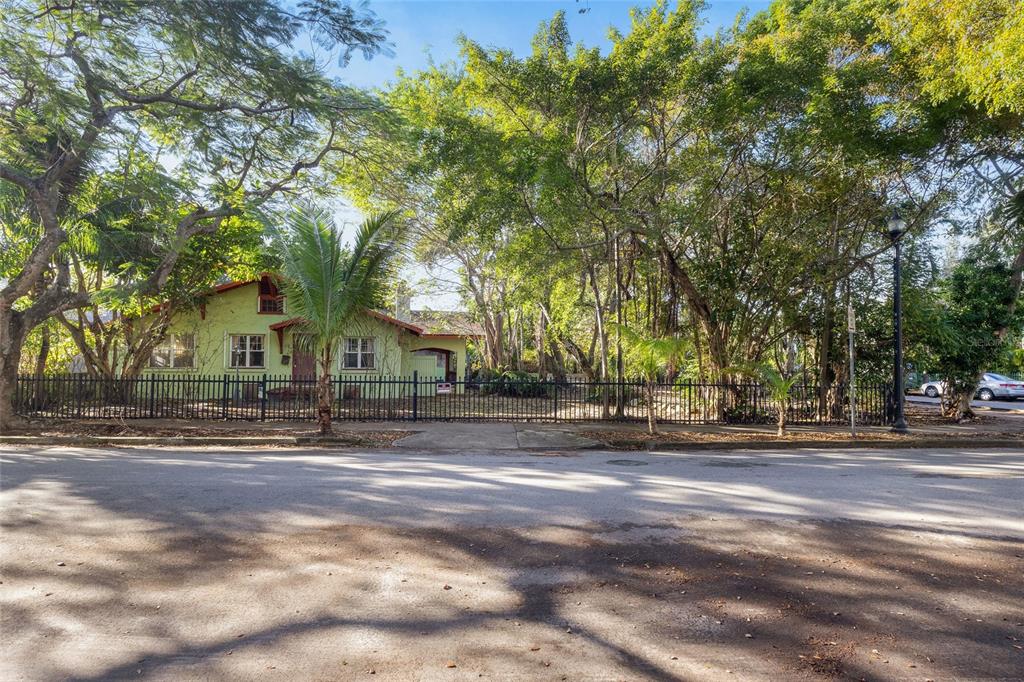 A light green house with a dark fence sits behind trees along a paved street — 58 NE 48TH STREET, MIAMI, FL