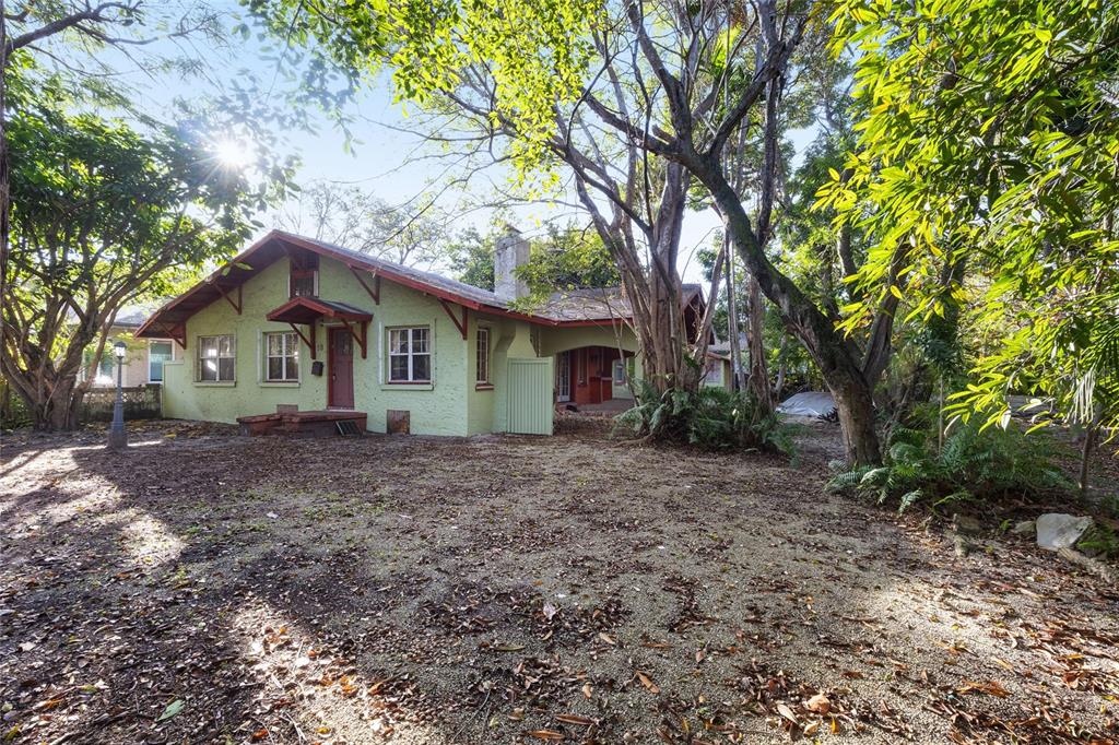 A light green, single-story house with a gabled roof sits in a wooded, leaf-covered yard — 58 NE 48TH STREET, MIAMI, FL