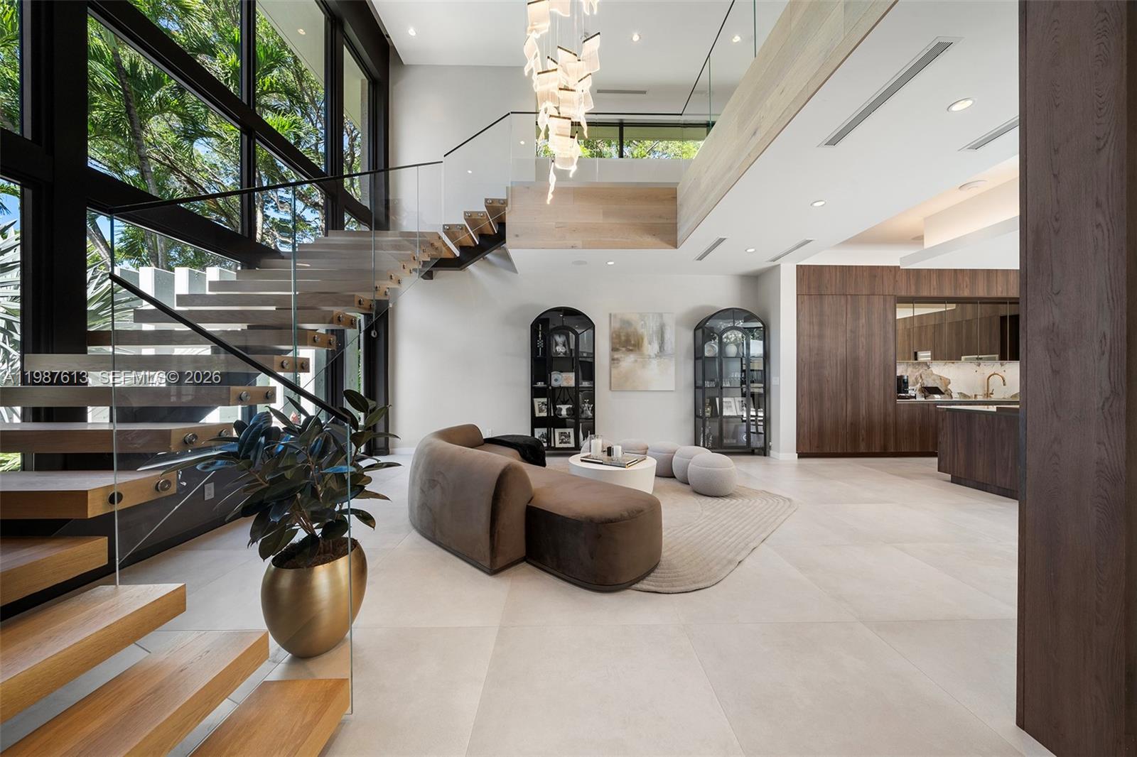 A modern living room features a floating wooden staircase, floor-to-ceiling windows, and a curved sofa — 4041 S Le Jeune Rd, Miami FL 33146, MIAMI, FL