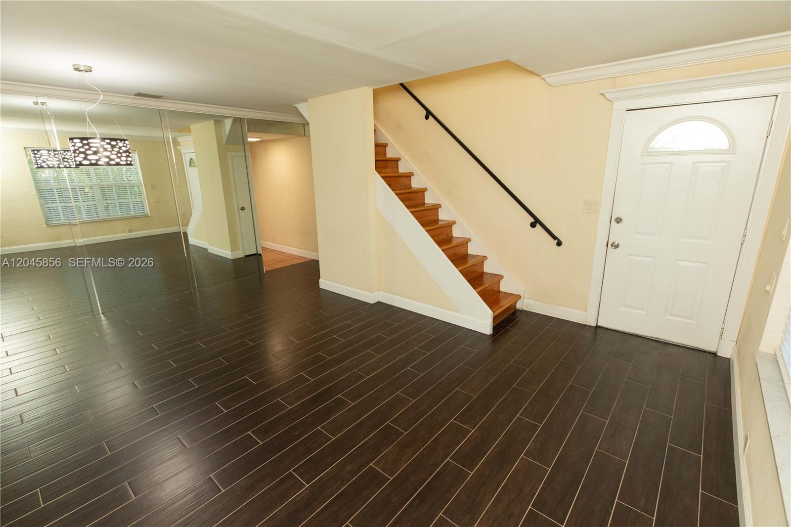 A room with dark wood-look tile flooring, a wooden staircase, and a white front door — 2945 Day Ave # 2953, Miami FL 33133, MIAMI, FL