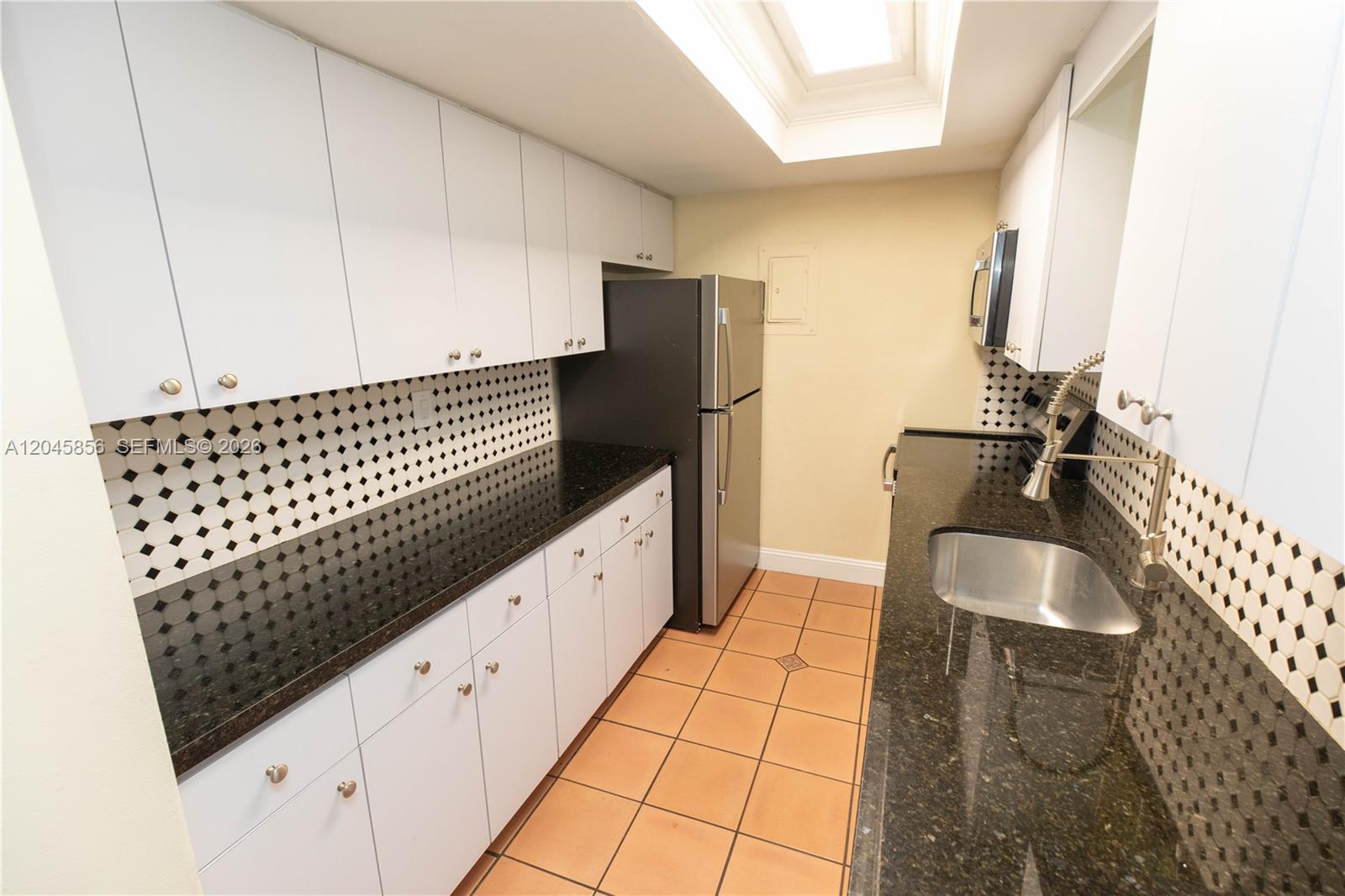 A galley kitchen features white cabinets, black granite countertops, a tiled backsplash, and terracotta flooring — 2945 Day Ave # 2953, Miami FL 33133, MIAMI, FL