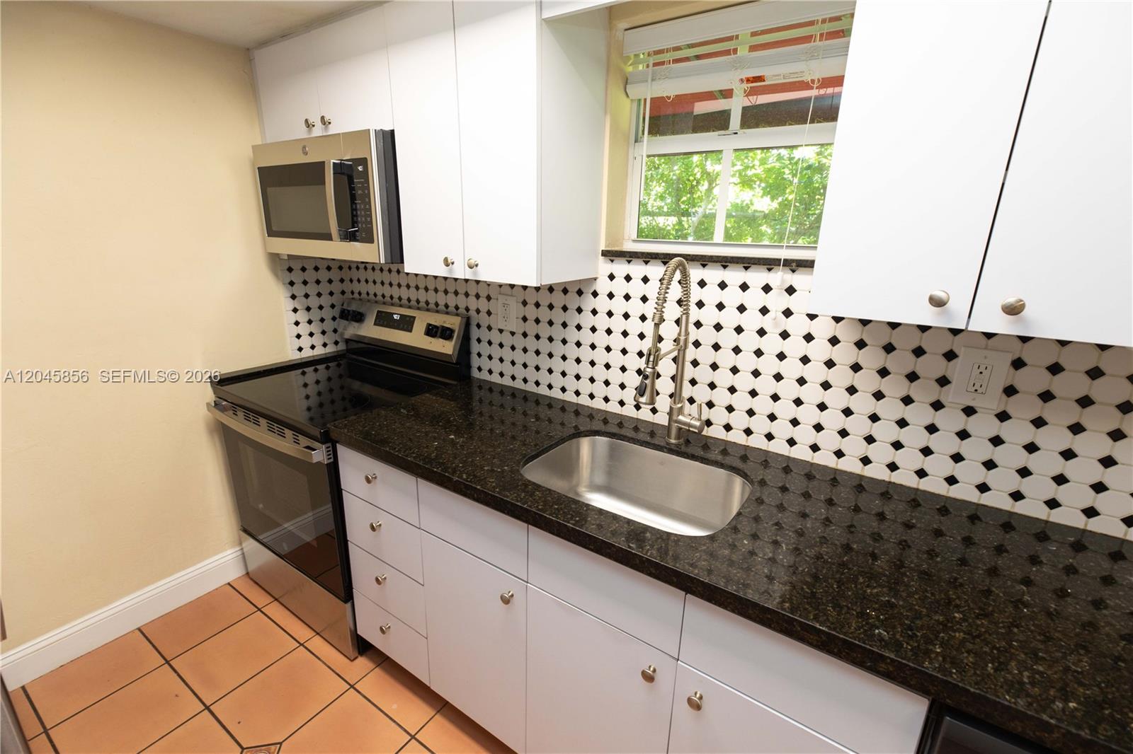 A kitchen features white cabinets, dark granite countertops, a stainless steel sink, and patterned tile — 2945 Day Ave # 2953, Miami FL 33133, MIAMI, FL