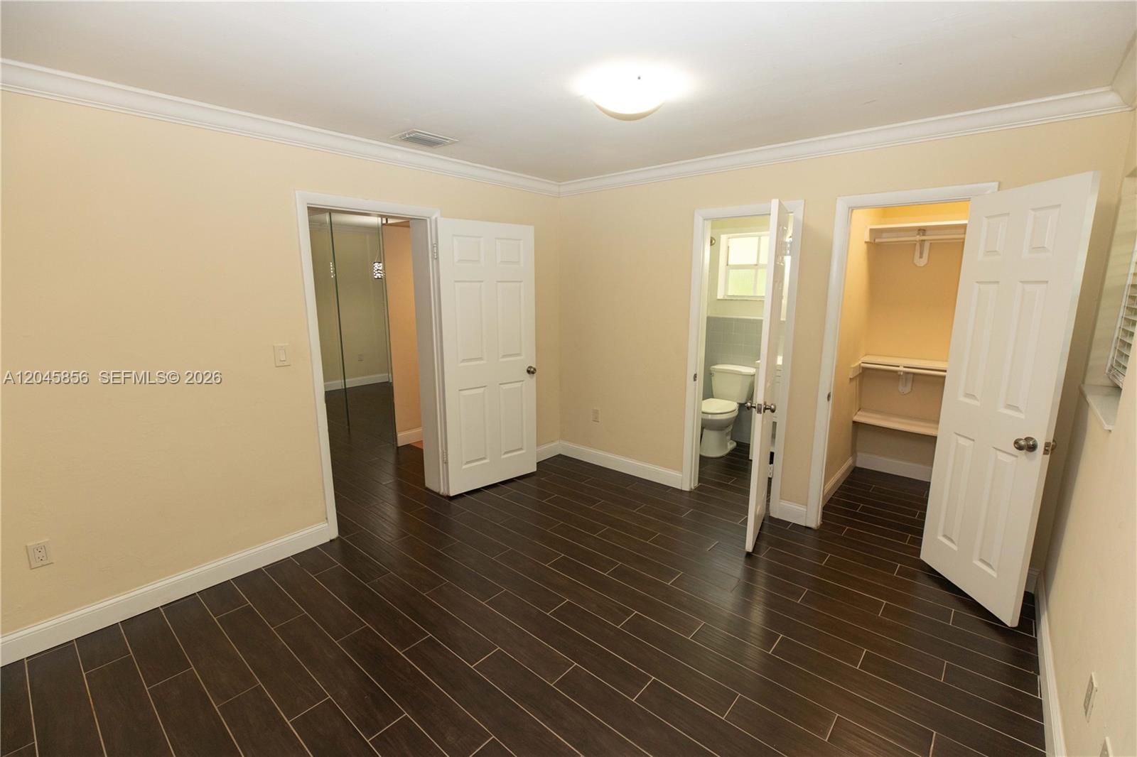This bedroom features dark wood-look tile flooring, beige walls, two white doors, and a closet — 2945 Day Ave # 2953, Miami FL 33133, MIAMI, FL