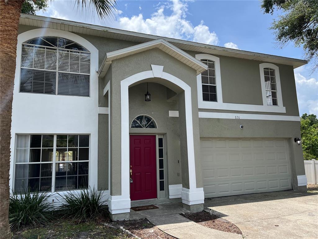 A two-story house with a beige stucco exterior, a red front door, and a garage — 820 STONECHAPEL COURT, APOPKA, FL
