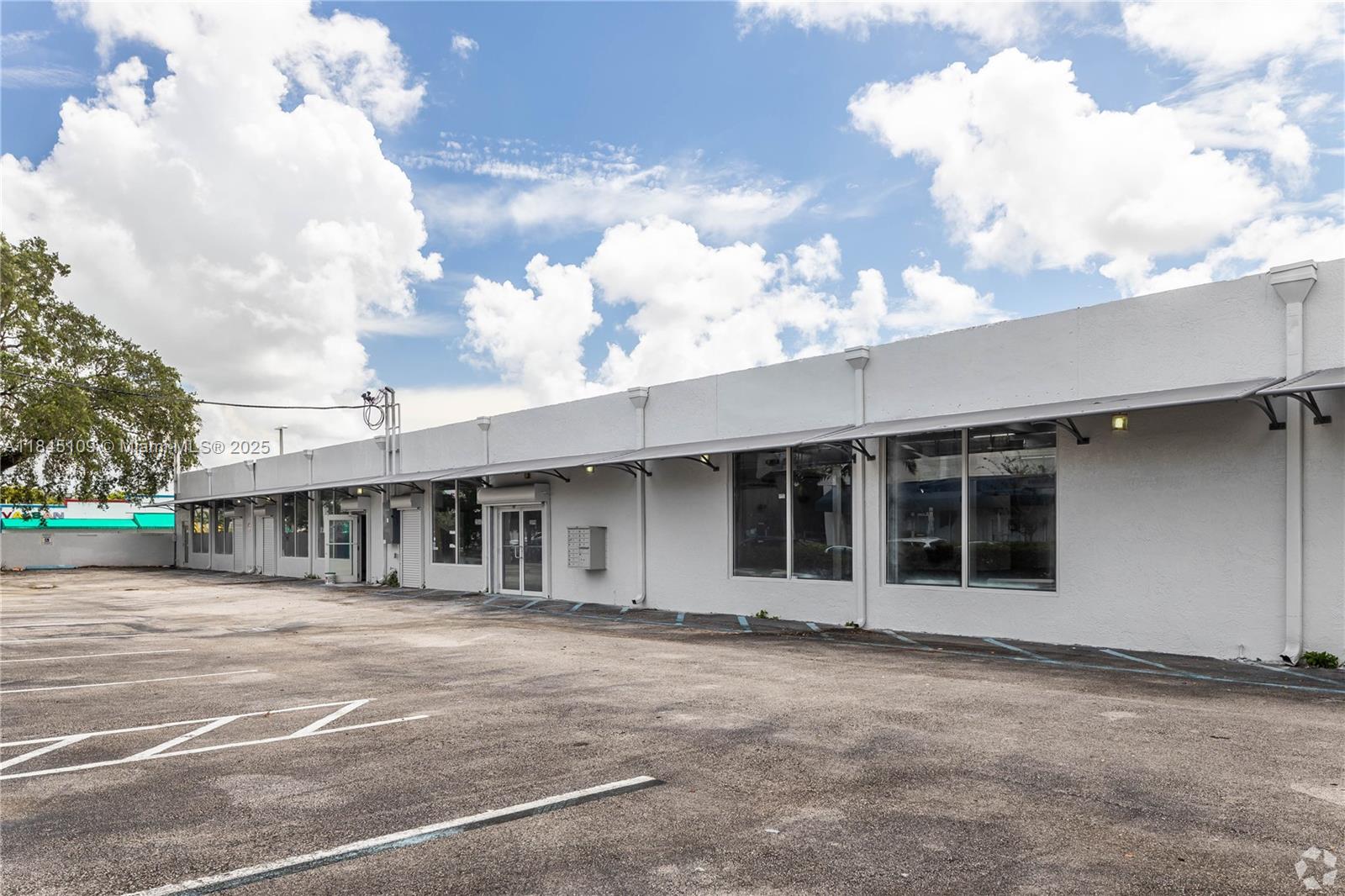 A single-story commercial building with a white stucco facade and a large asphalt parking lot — 2090 NW 21st St, Miami FL 33142, MIAMI, FL