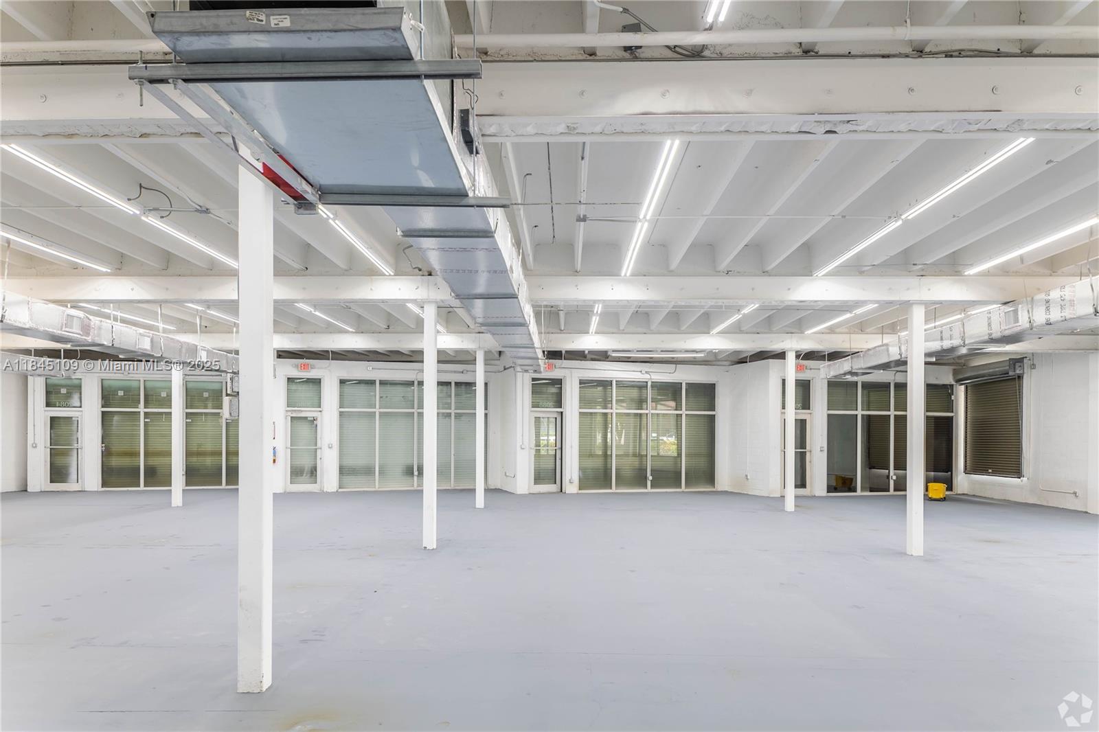 An empty commercial space features white support columns, exposed ceiling beams, and large glass windows — 2090 NW 21st St, Miami FL 33142, MIAMI, FL