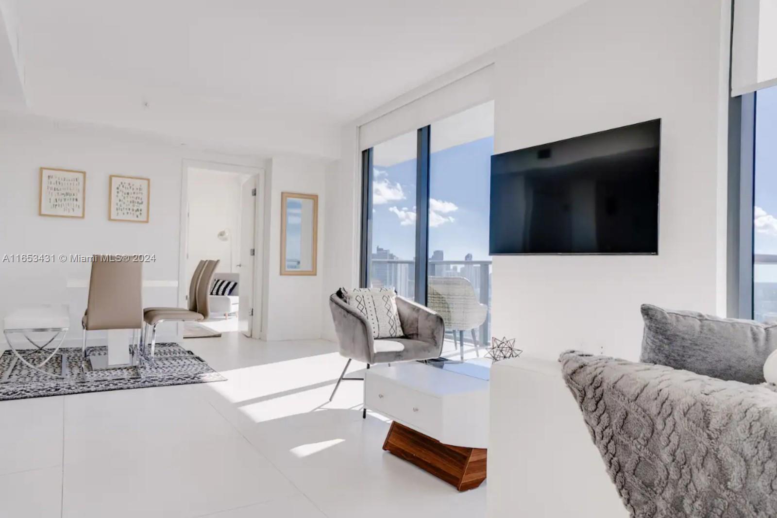 A bright, modern living room features white flooring, a wall-mounted television, and floor-to-ceiling windows — 501 NE 31st St # 3709, Miami FL 33137, MIAMI, FL