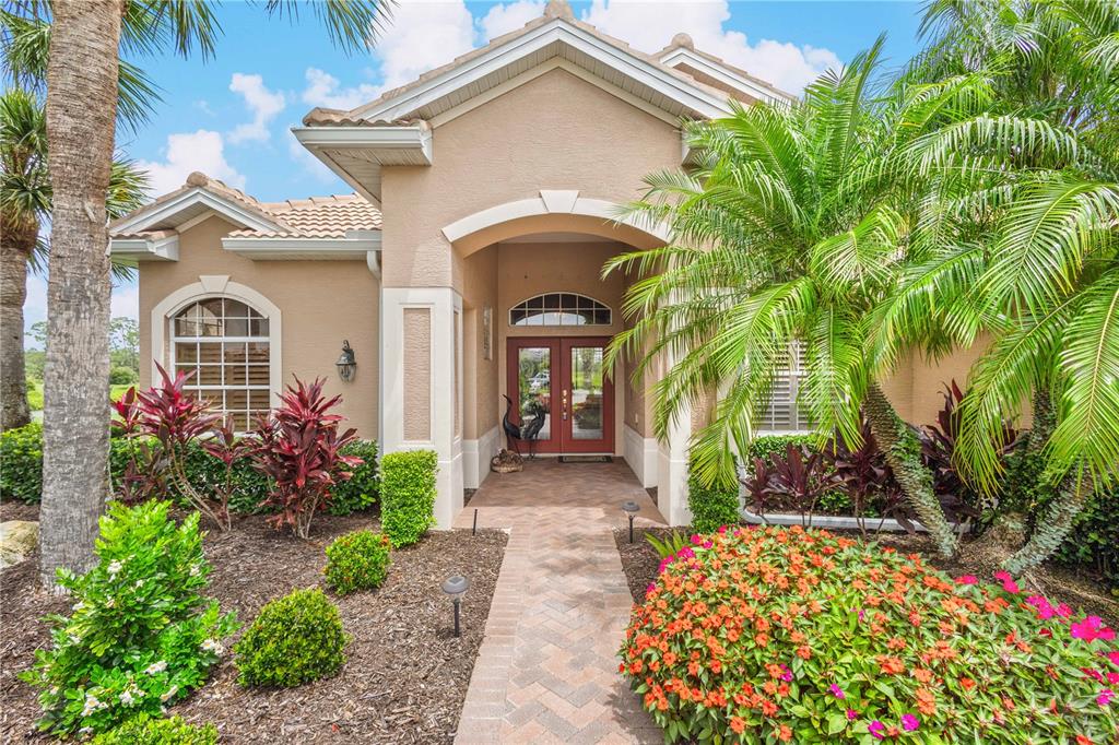 A beige house exterior features a brick walkway leading to a double front door entrance — 5302 WHITE IBIS CT., NORTH PORT, FL