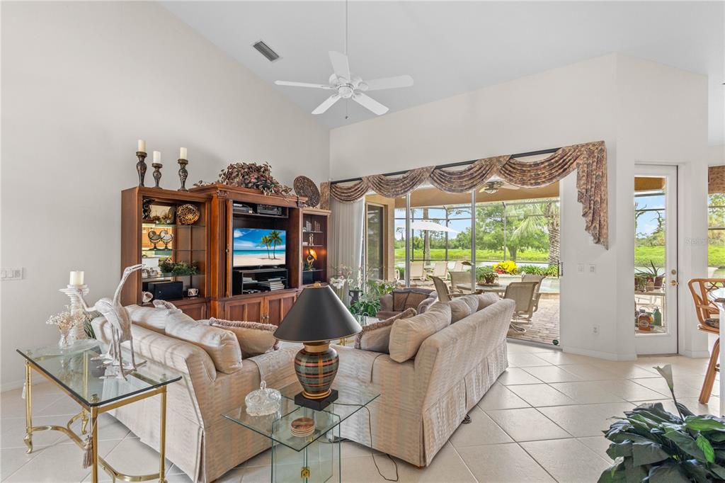 A living room with a vaulted ceiling, beige sofa, entertainment center, and sliding glass doors — 5302 WHITE IBIS CT., NORTH PORT, FL