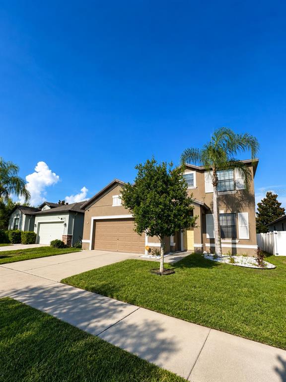 A two-story suburban house with a tan stucco exterior, a garage, and a palm tree — 10908 WHITTNEY CHASE DRIVE, RIVERVIEW, FL
