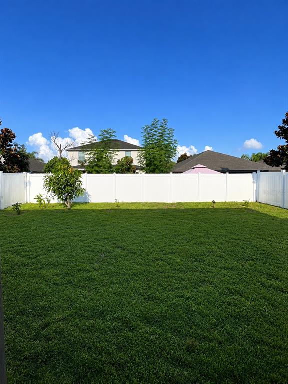 A grassy backyard features a white vinyl privacy fence and several small trees — 10908 WHITTNEY CHASE DRIVE, RIVERVIEW, FL