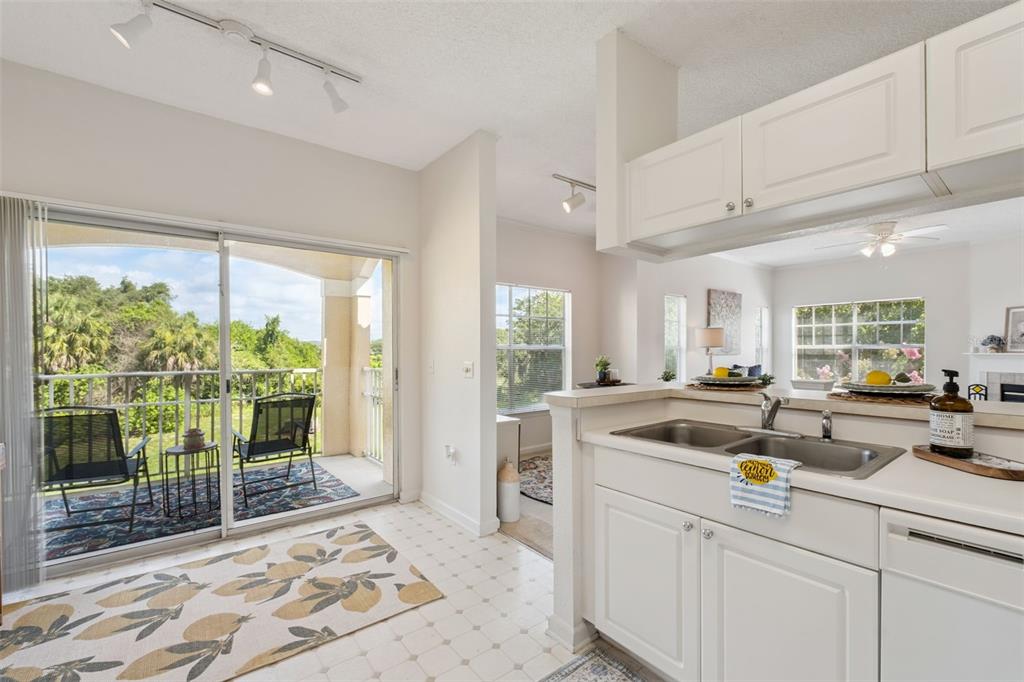 A kitchen with white cabinets and a double sink overlooks a balcony with outdoor seating — 426 ARBOR LAKES UNIT 426, SANFORD, FL