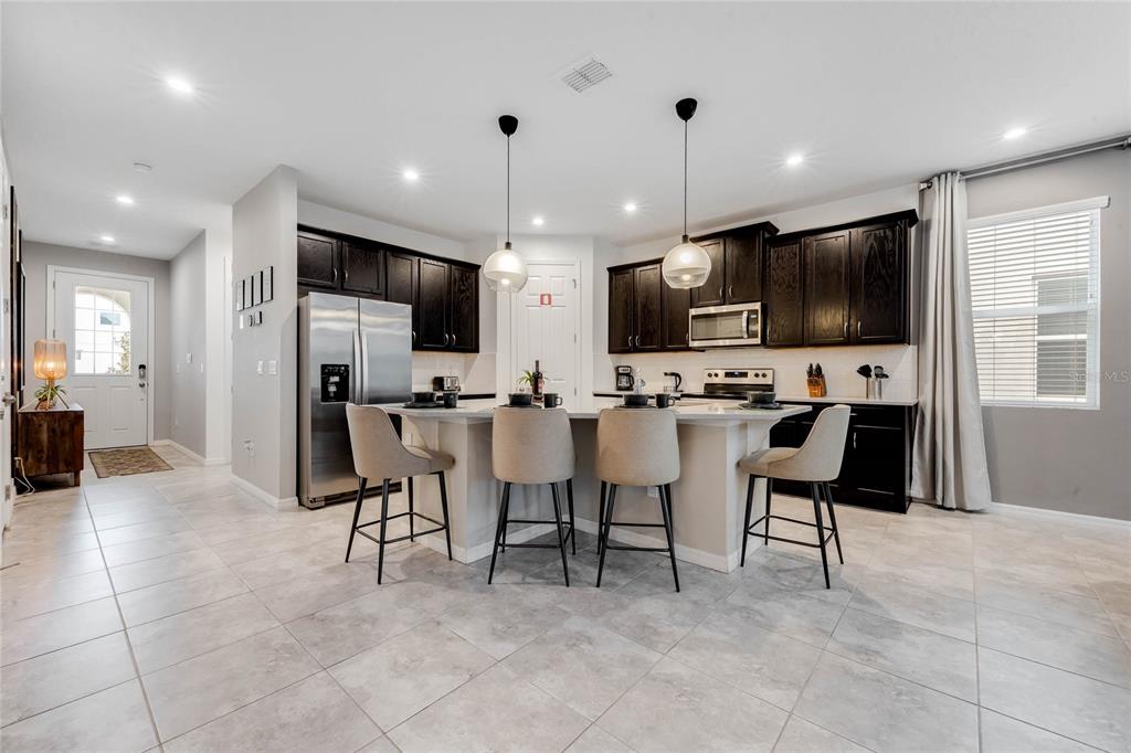A kitchen features dark cabinets, a central island with four stools, and light tile flooring — 8943 AMELIA DOWNS TRAIL, KISSIMMEE, FL