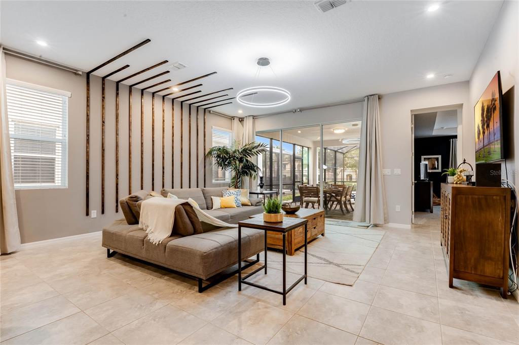 A living room features a sectional sofa, a wood-slat accent wall, and sliding glass doors — 8943 AMELIA DOWNS TRAIL, KISSIMMEE, FL