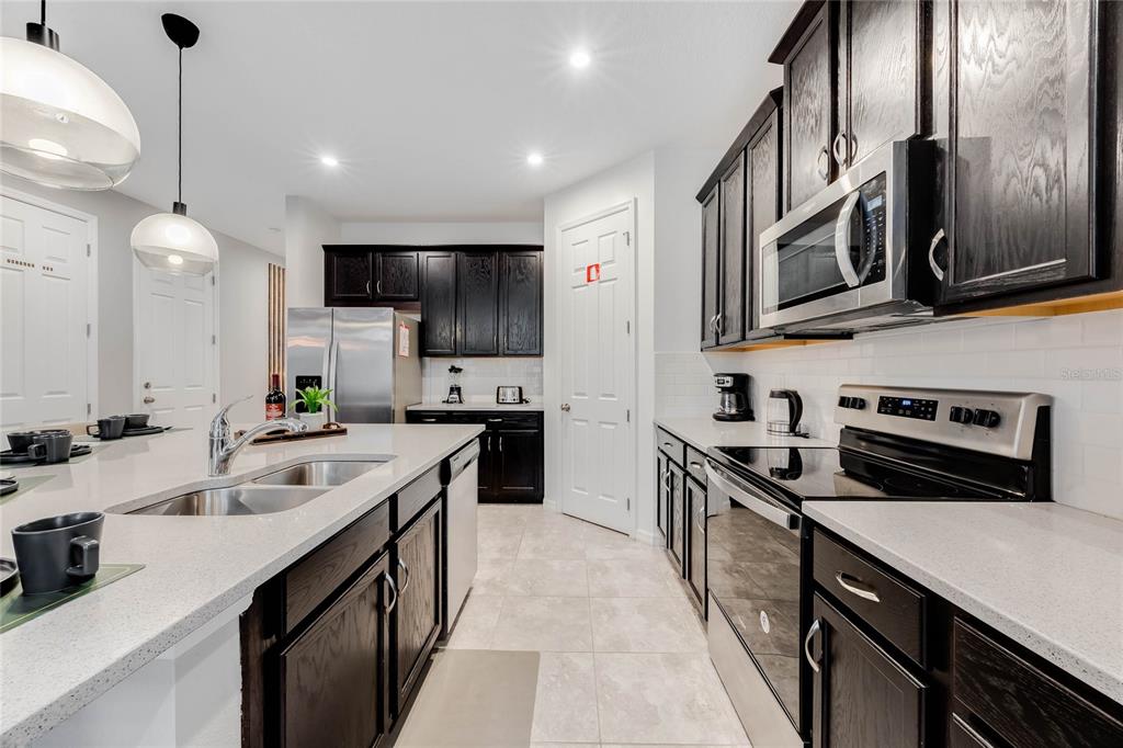 A kitchen features dark wood cabinets, white countertops, stainless steel appliances, and a central island — 8943 AMELIA DOWNS TRAIL, KISSIMMEE, FL