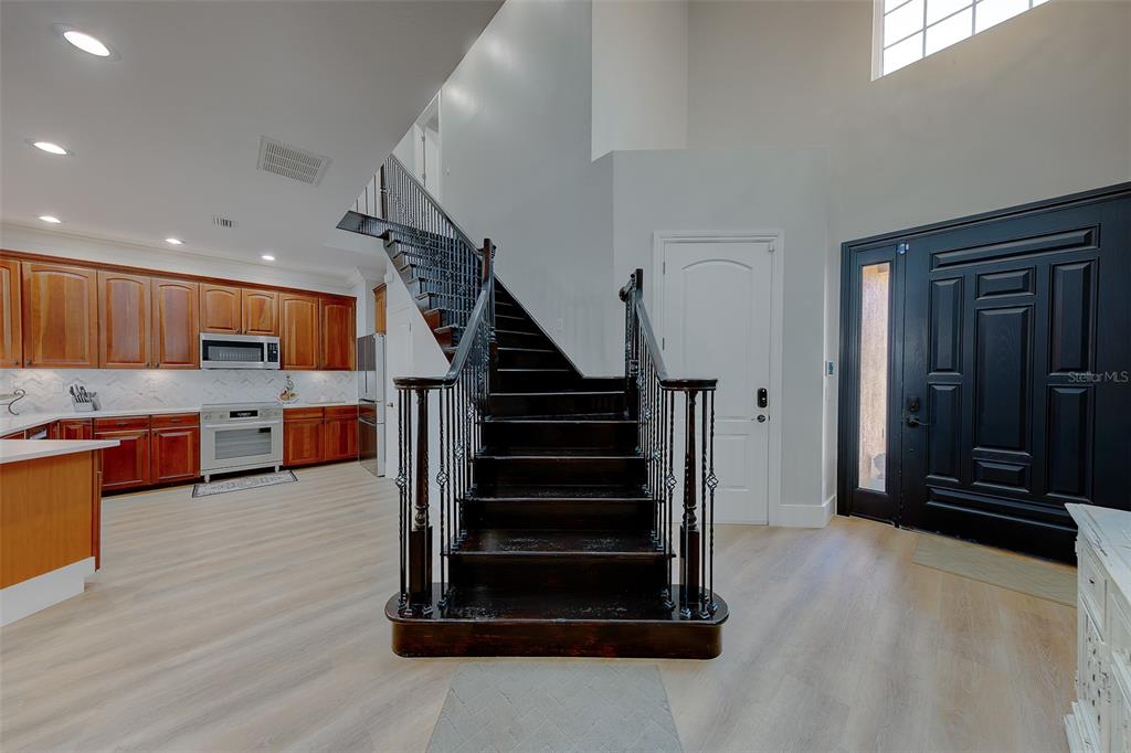 A foyer features a dark wood staircase, light wood flooring, and an adjacent open-concept kitchen — 1415 TESSANO PLACE, PALM HARBOR, FL