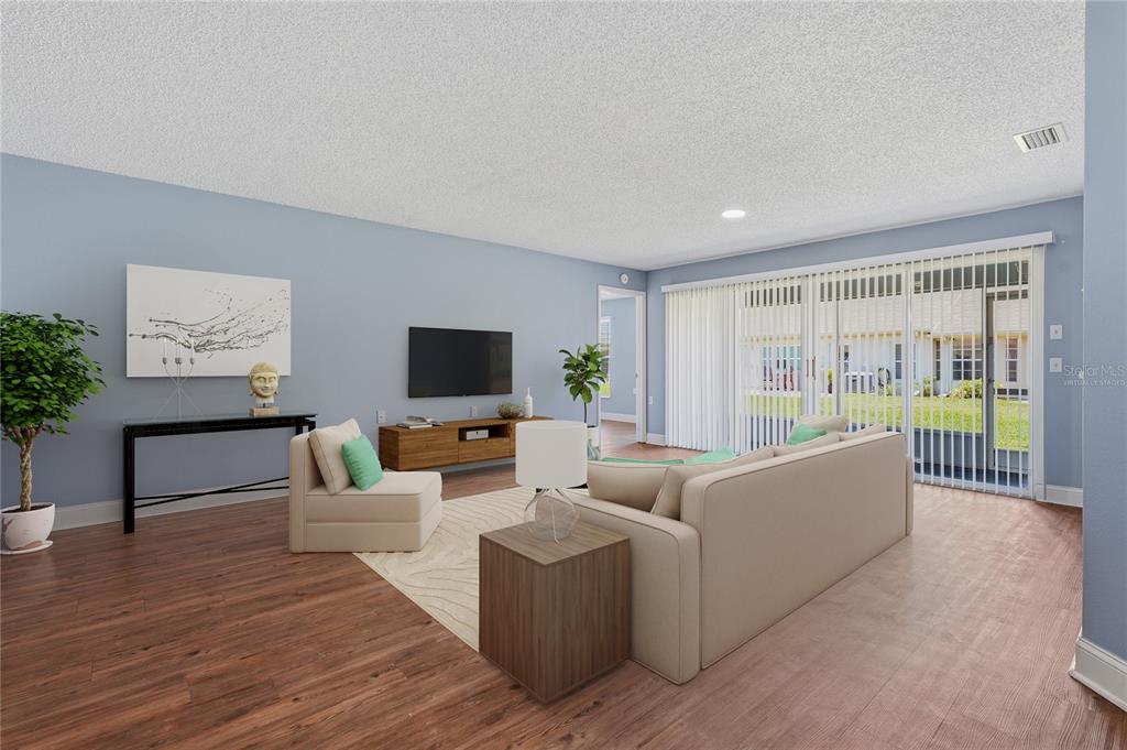 A living room with light blue walls, wood-look flooring, a sofa, and sliding glass doors — 9031 WARWICK LANE UNIT 9031, NEW PORT RICHEY, FL