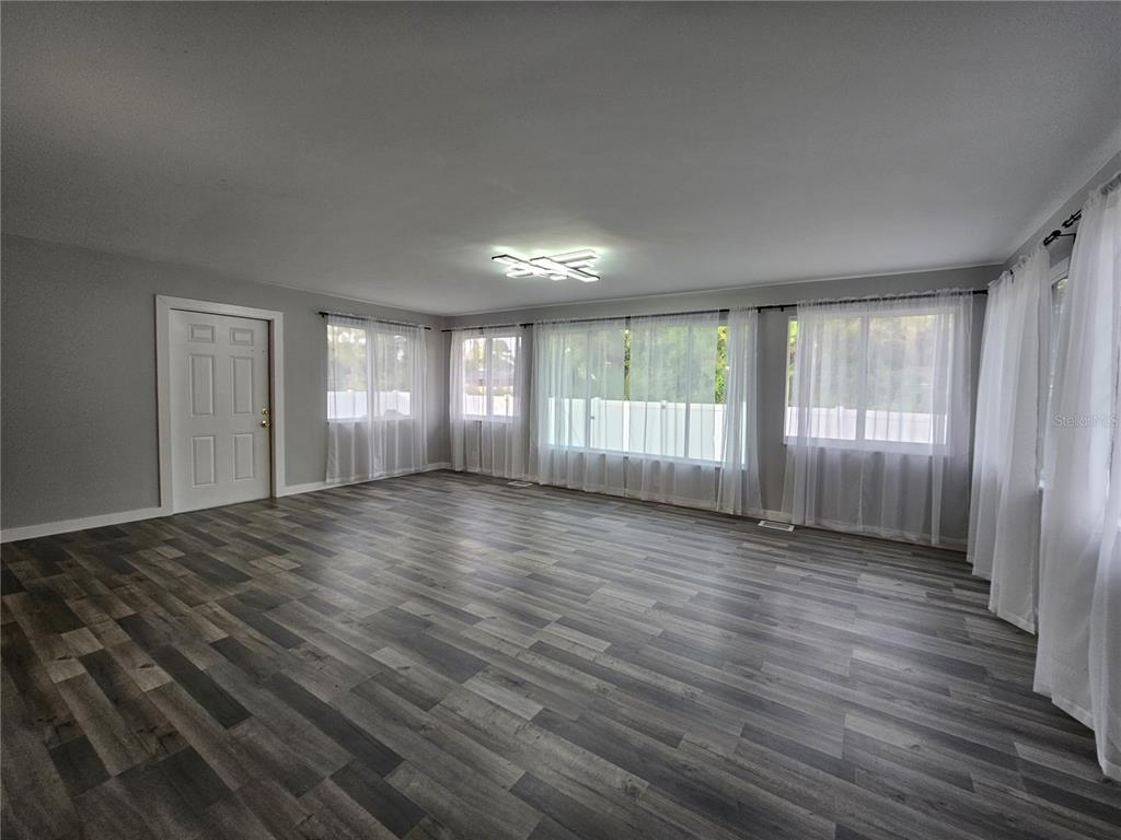 A spacious living room features gray wood-look flooring, light gray walls, and large windows with curtains — 2321 INGRAM AVENUE, SARASOTA, FL