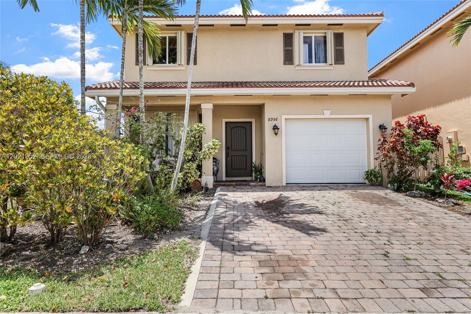A two-story stucco house features a brick paver driveway, a garage, and tropical landscaping — 8956 SW 215th Ter, Cutler Bay FL 33189, CUTLER BAY, FL