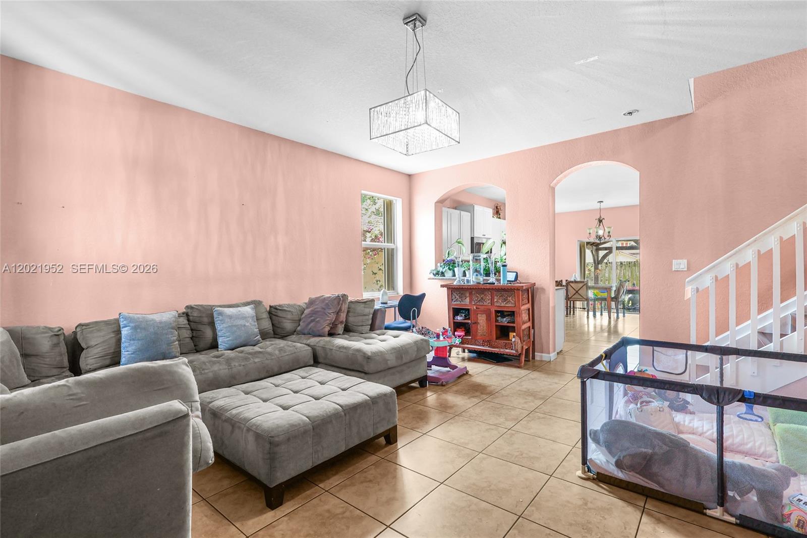 A living room features a large gray sectional, tile flooring, and pink walls — 8956 SW 215th Ter, Cutler Bay FL 33189, CUTLER BAY, FL