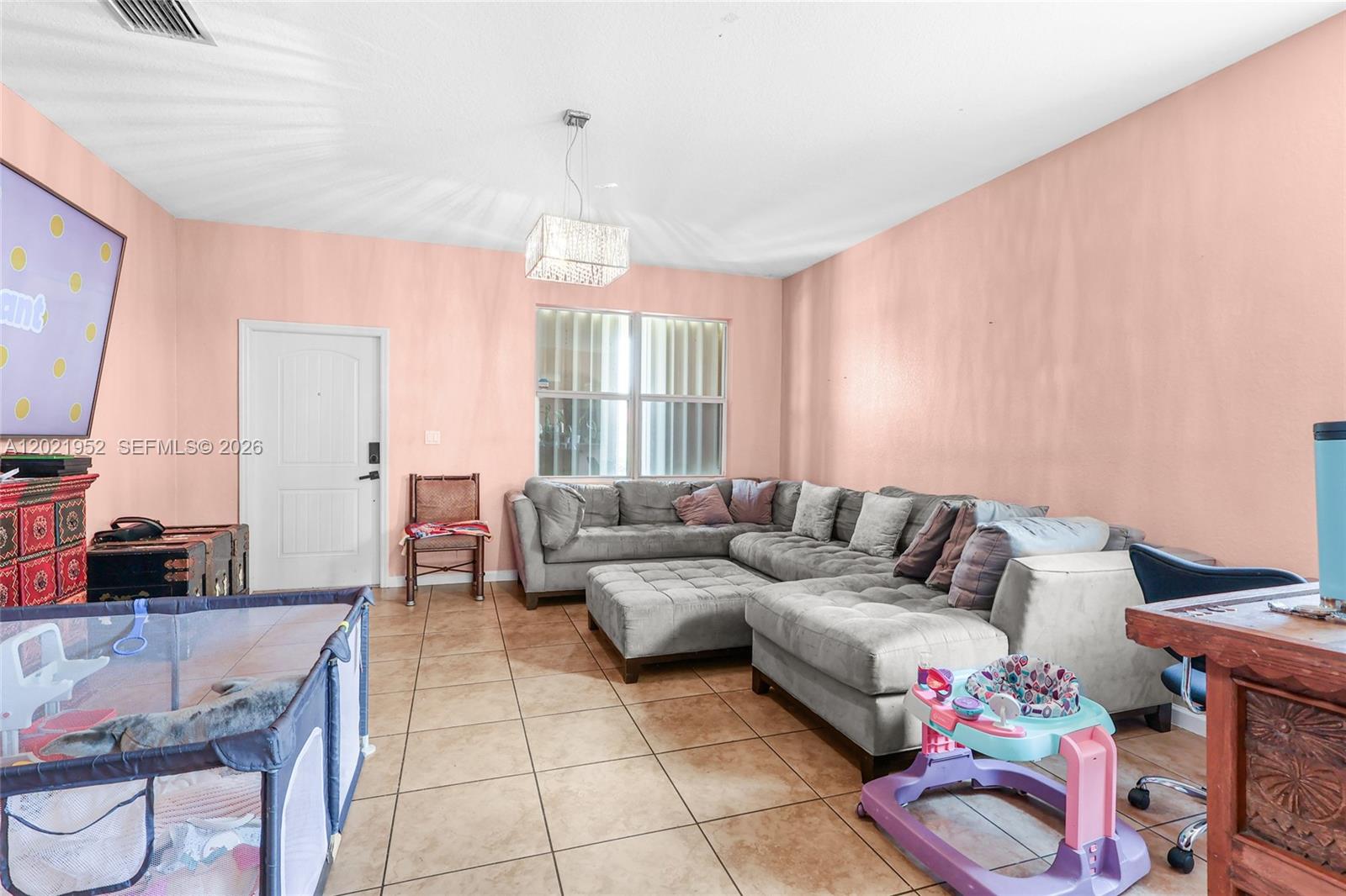 A living room features peach walls, tile flooring, a large gray sectional, and a chandelier — 8956 SW 215th Ter, Cutler Bay FL 33189, CUTLER BAY, FL