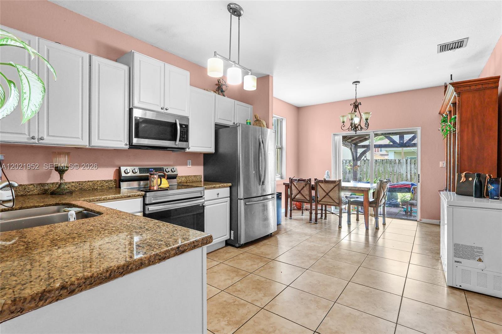 A kitchen with granite countertops, white cabinets, and stainless steel appliances opens to a dining area — 8956 SW 215th Ter, Cutler Bay FL 33189, CUTLER BAY, FL