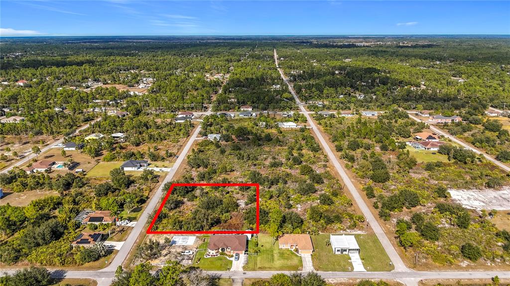 An aerial view shows a vacant, rectangular residential lot outlined in red among suburban homes — 904 LAKE AVENUE, LEHIGH ACRES, FL