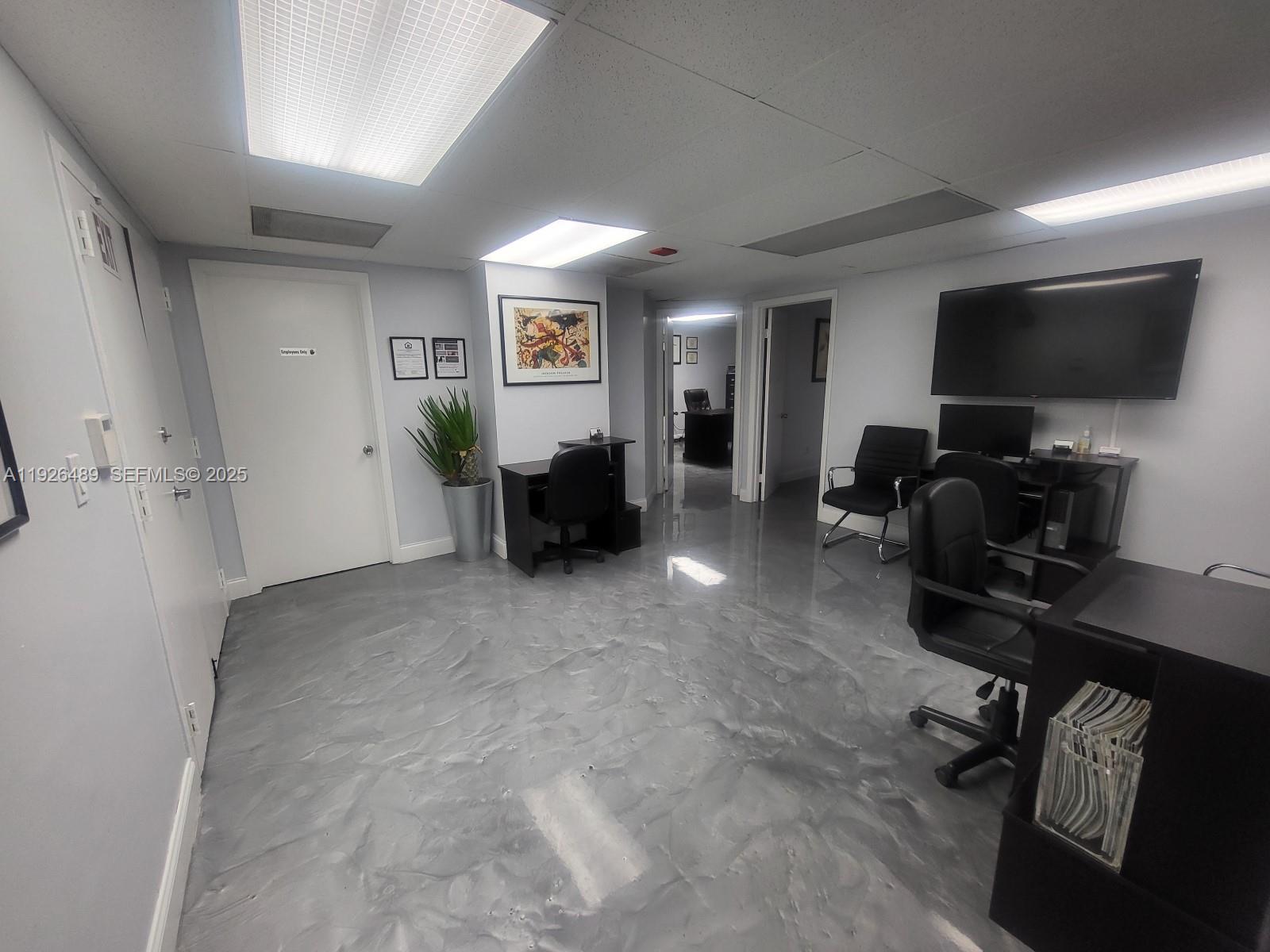 An office space features gray epoxy flooring, several desks with chairs, and a wall-mounted television — 13499 Biscayne Blvd, North Miami FL 33181, NORTH MIAMI, FL
