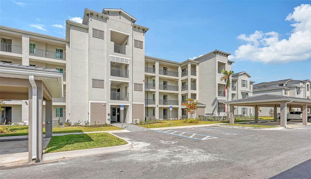 An exterior view of a multi-story apartment building with covered parking and accessible parking spaces — 12280 WELLEN GOLF STREET UNIT 308, VENICE, FL
