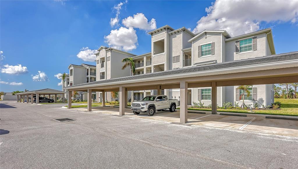 A multi-story apartment building features covered parking spaces and a white pickup truck — 12280 WELLEN GOLF STREET UNIT 308, VENICE, FL
