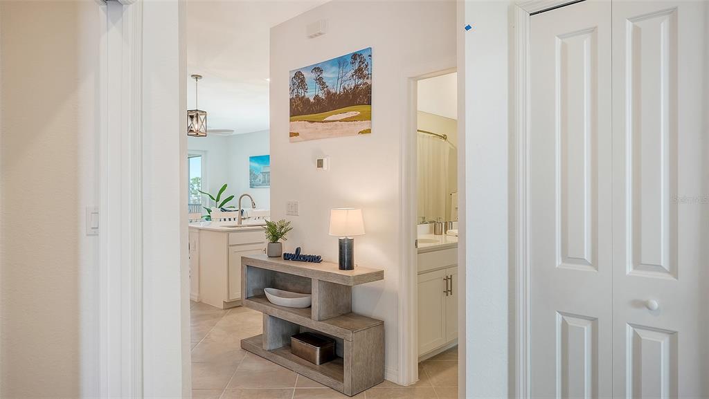 A foyer with a console table and wall art leads into a kitchen with white cabinets — 12280 WELLEN GOLF STREET UNIT 308, VENICE, FL