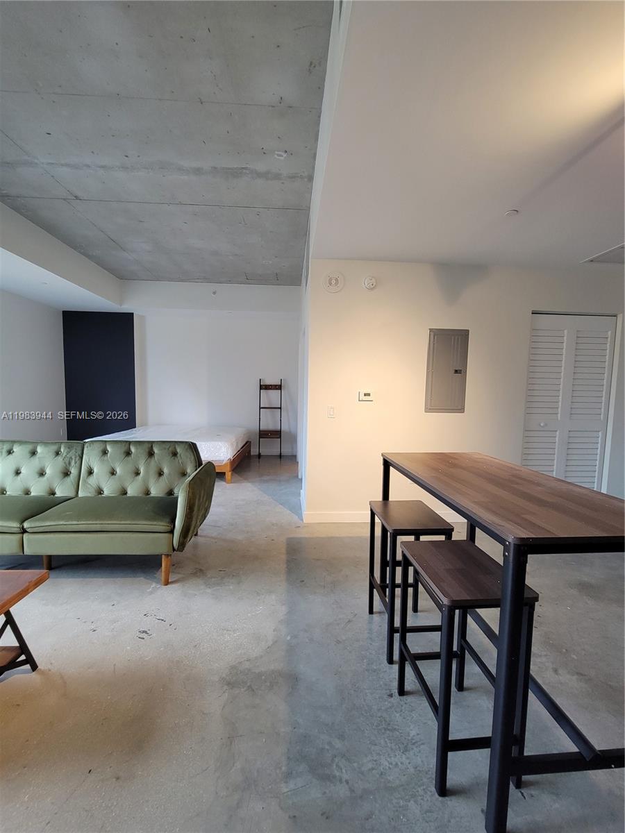 This studio apartment features a concrete ceiling, polished concrete floors, a green sofa, and a dining table — 151 SE 1st St # 1507, Miami FL 33131, MIAMI, FL