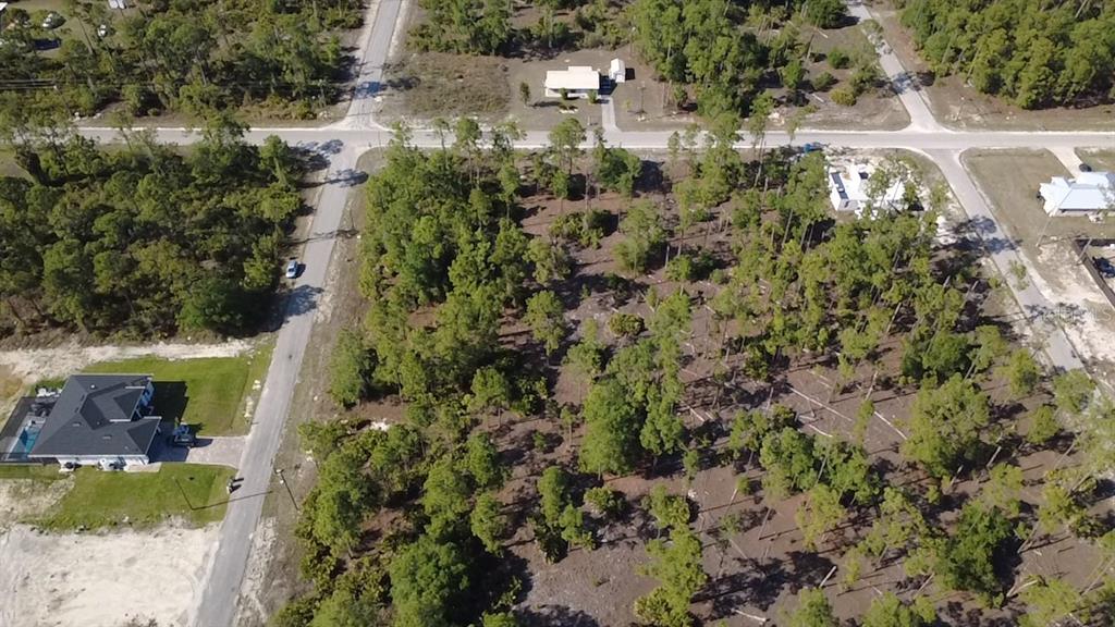 An aerial view shows a wooded, undeveloped residential lot surrounded by paved roads and houses — 920 LOUIS AVENUE, LEHIGH ACRES, FL