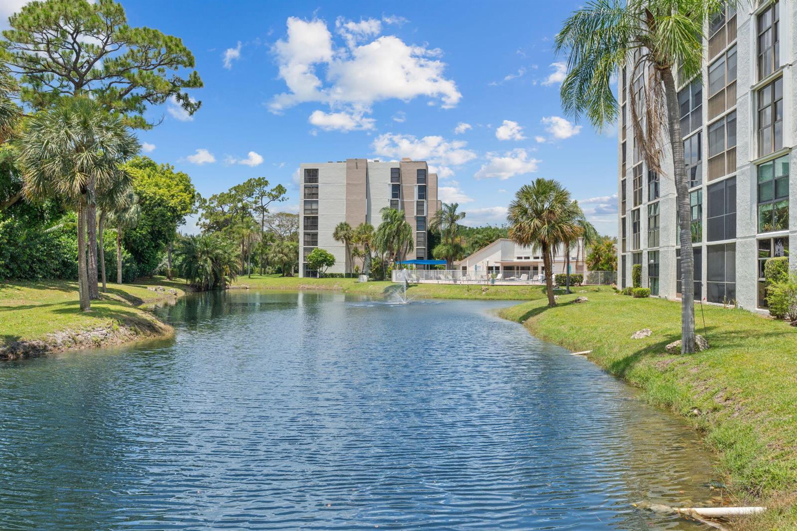 A pond sits between two multi-story apartment buildings with palm trees and a swimming pool — 6562 Boca Del Mar Drive # 124, Boca Raton FL 33433, BOCA RATON, FL