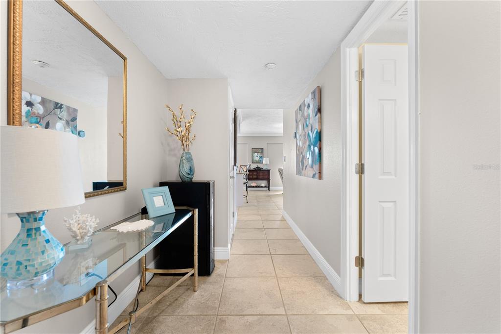 A hallway with tile flooring leads toward a distant room, featuring a glass console table — 1700 BENJAMIN FRANKLIN DRIVE UNIT 10F, SARASOTA, FL
