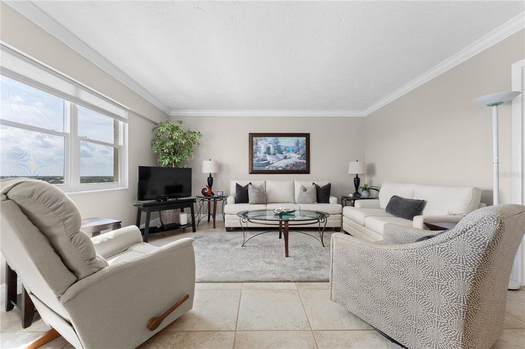 A living room features a sofa, armchairs, a coffee table, and a television near windows — 1700 BENJAMIN FRANKLIN DRIVE UNIT 10F, SARASOTA, FL