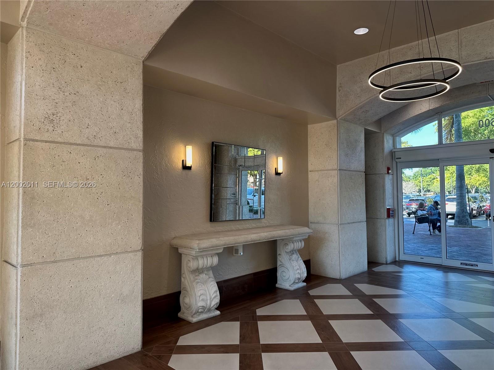 A lobby features a stone console table, a mirror, wall sconces, and tiled flooring — MIAMI LAKES, FL