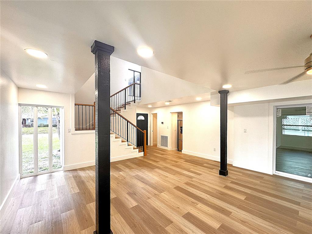 A living room with wood-look flooring, a vaulted ceiling, and a staircase with wooden treads — 14 GLENDALE DRIVE, KISSIMMEE, FL