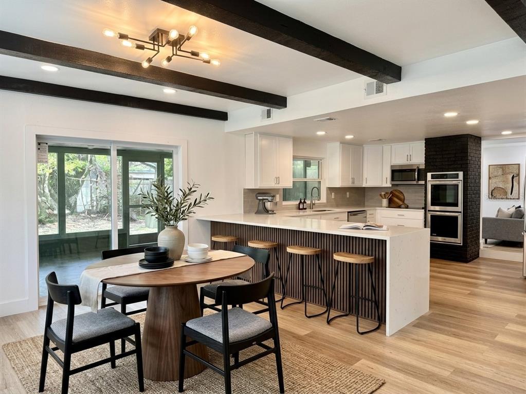 A bright, open-concept living area features light wood flooring, two black support columns, and stairs — 14 GLENDALE DRIVE, KISSIMMEE, FL