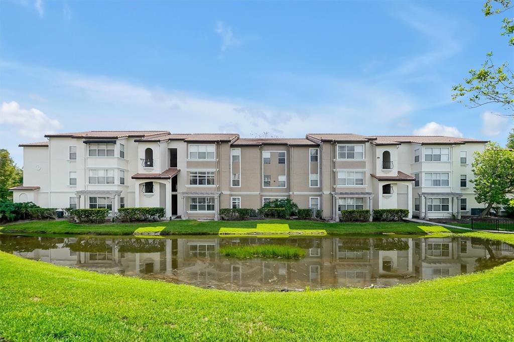 A multi-story apartment building sits behind a grassy lawn and a small pond — 5156 CONROY ROAD UNIT 26, ORLANDO, FL