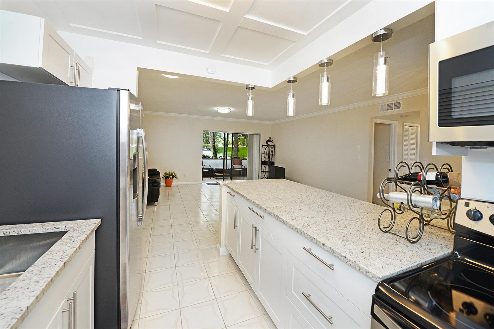 A kitchen with white cabinets, granite countertops, and stainless steel appliances overlooks a living area — 297 Deer Creek Boulevard # 1302, Deerfield Beach FL 33442, DEERFIELD BEACH, FL