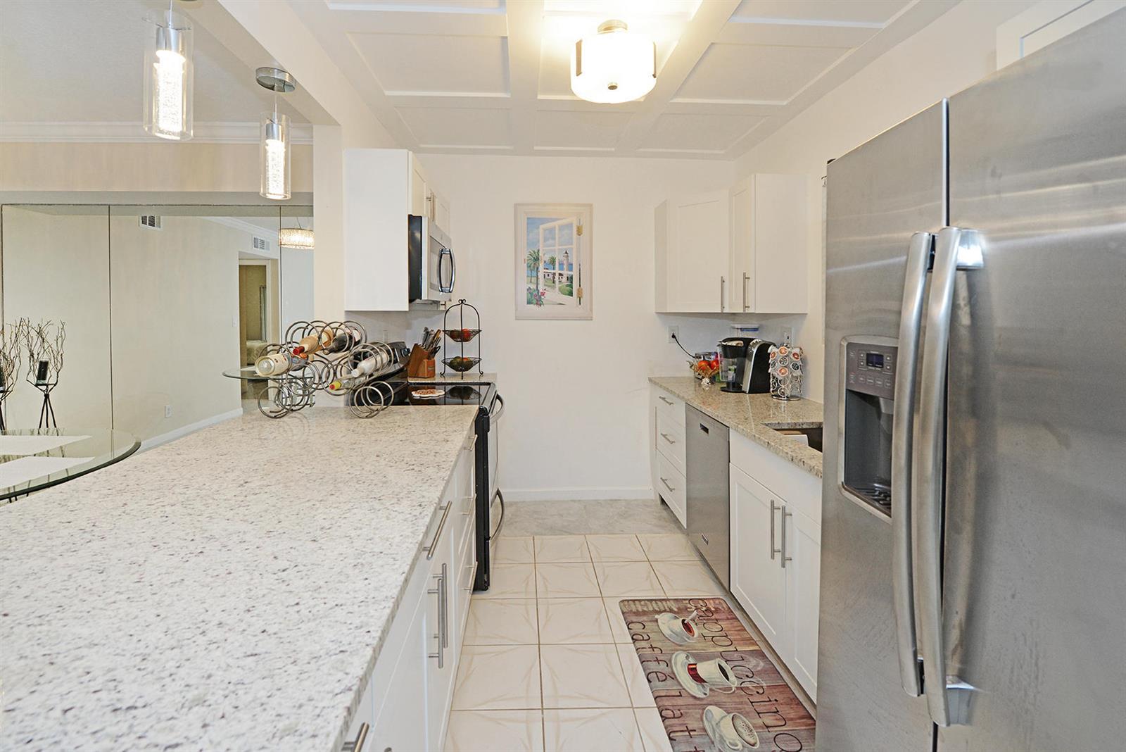 A galley kitchen features white cabinets, granite countertops, stainless steel appliances, and tile flooring — 297 Deer Creek Boulevard # 1302, Deerfield Beach FL 33442, DEERFIELD BEACH, FL