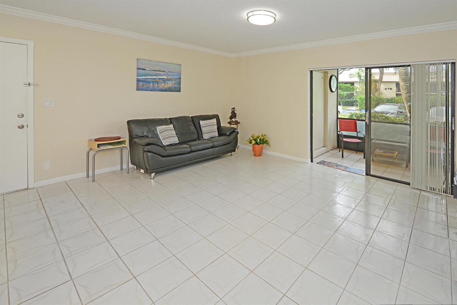 A living room with light tile flooring, a dark sofa, and a sliding glass door — 297 Deer Creek Boulevard # 1302, Deerfield Beach FL 33442, DEERFIELD BEACH, FL