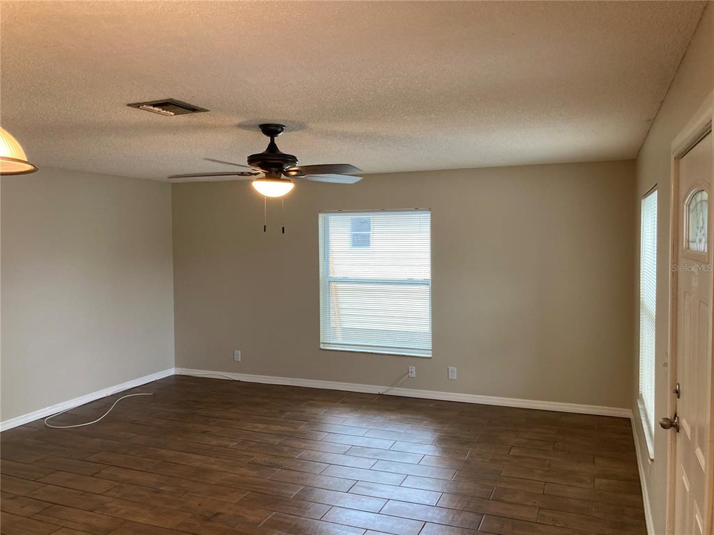 A living room with wood-look tile flooring, a ceiling fan, and a single window — 7112 2ND STREET N, ST PETERSBURG, FL