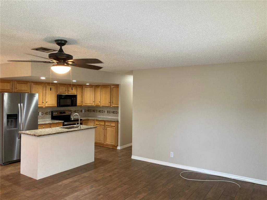 A kitchen with wood cabinets and granite countertops opens into a living area with flooring — 7112 2ND STREET N, ST PETERSBURG, FL