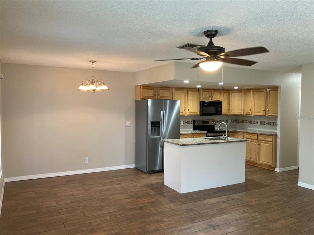 A kitchen with light wood cabinets, granite countertops, a center island, and wood-look flooring — 7112 2ND STREET N, ST PETERSBURG, FL