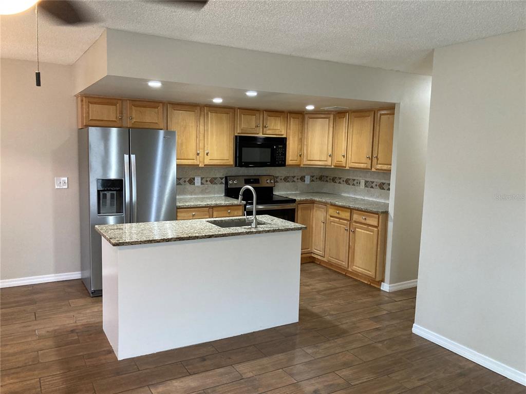A kitchen features light wood cabinets, granite countertops, stainless steel appliances, and a central island — 7112 2ND STREET N, ST PETERSBURG, FL