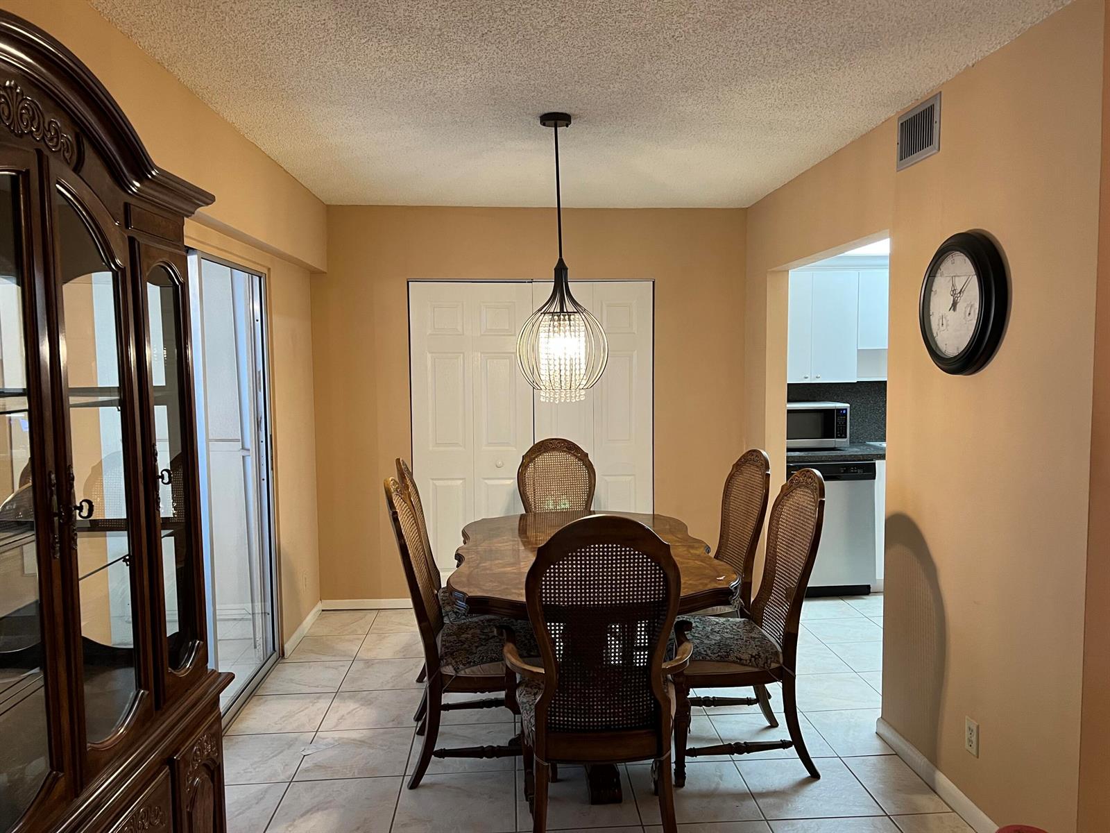 A dining room with a wooden table, cane-back chairs, a crystal pendant light, and tile flooring — 203 Suffolk, Boca Raton FL 33434, BOCA RATON, FL